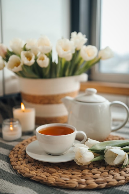 Tasse Tee Teekannenkorb mit Tulpenkerzen im ästhetischen Foto des Innenraums