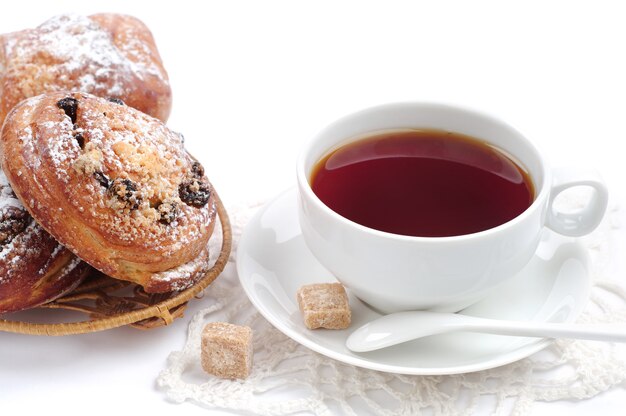 Tasse Tee und Brötchen mit Rosinen auf weißem Hintergrund