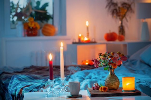 Tasse Tee und Chrysantheme in Vase mit brennenden Kerzen im Schlafzimmer