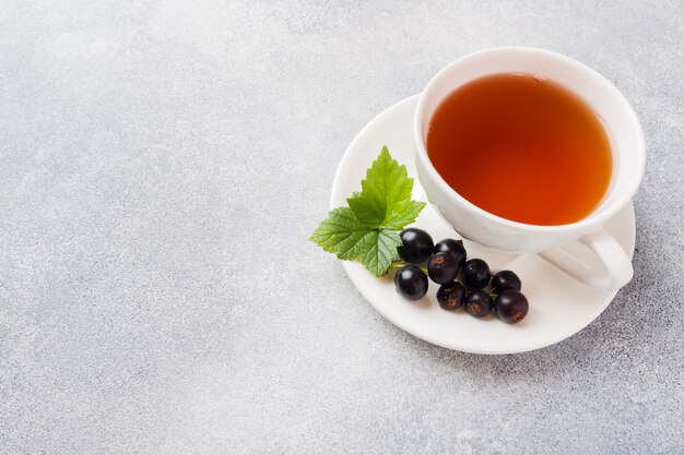 Tasse Tee und frische Beeren der schwarzen Johannisbeere auf grauer Tabelle. Kopieren Sie Platz.