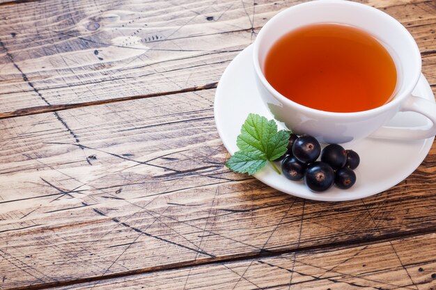 Tasse Tee und frische Beeren der schwarzen Johannisbeere auf hölzernem. Kopieren Sie Platz.