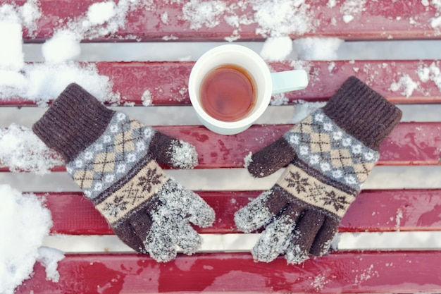 Tasse Tee und gestrickte Damenhandschuhe auf einer Bank Winter der Schnee unter Draufsicht