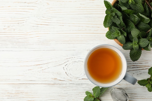 Tasse Tee und Minze auf weißem Holztisch, Platz für Text