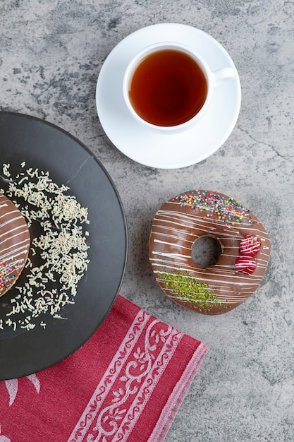 Tasse Tee und Schokoladenkrapfen mit Beeren und Streuseln auf Marmoroberfläche.