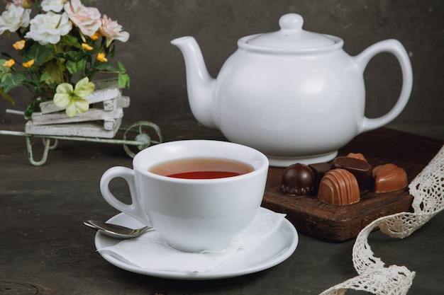 Tasse Tee und Teekanne und Pralinen auf dem schwarzen Hintergrund