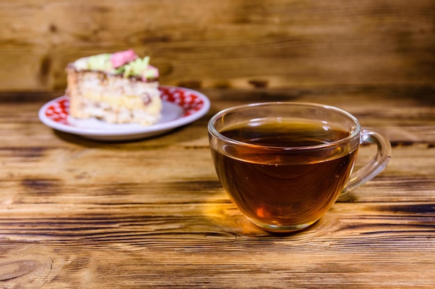 Tasse Tee und Teller mit Stück Kiewer Kuchen mit Sahnenüssen und Baiser auf einem Holztisch