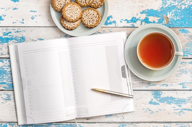 Tasse Tee und Untertasse mit Keksen mit Notizblock auf dem Tisch Draufsicht