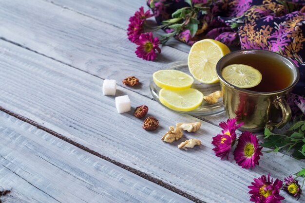 Tasse Tee, Zitrone und Blumen auf einem weißen Holztisch