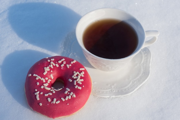 Tasse Tee zum Frühstück mit Donuts auf Schneehintergrund