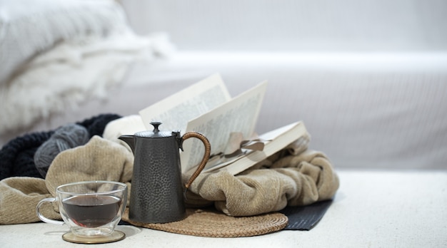 Tasse, Teekanne und Buch im Vordergrund in kalten Farben auf unscharfem Hintergrund.