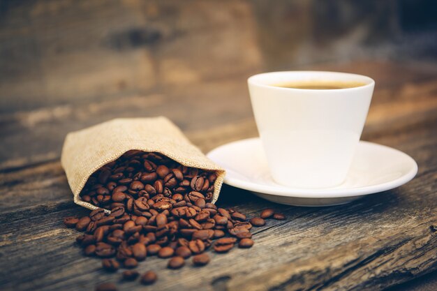 Tasse und Kaffeebohnen fallen auf einer alten Holzoberfläche aus dem Beutel