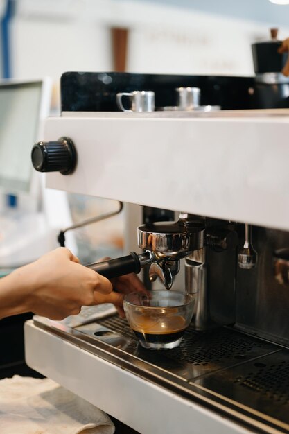 Tasse und professionelle Espresso-Maschine, die frischen Kaffee in einen Glasbecher gießt