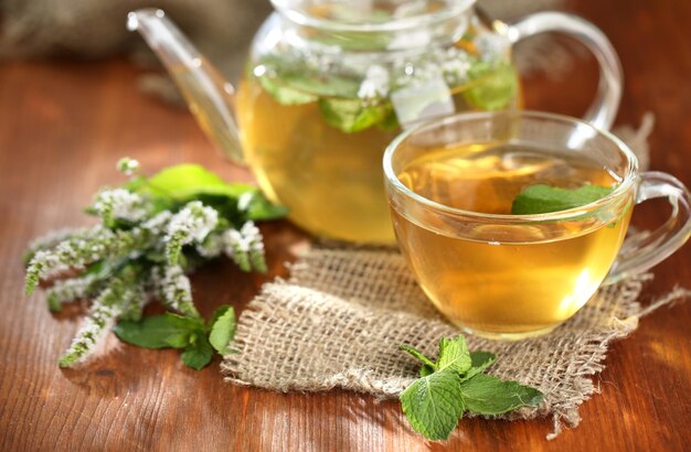 Tasse und Teekanne Kräutertee mit frischen Minzblumen auf Holztisch