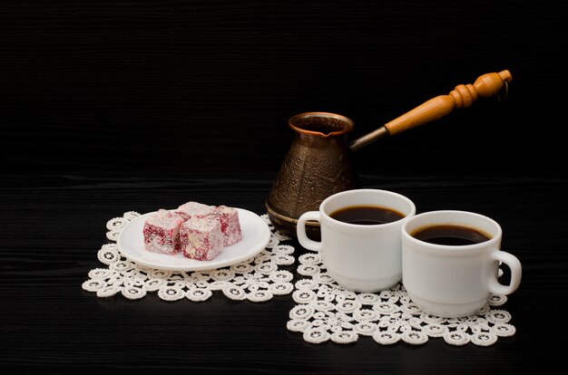 Tassen Kaffee, türkische Freude und Kirschtöpfe auf einem schwarzen Hintergrund