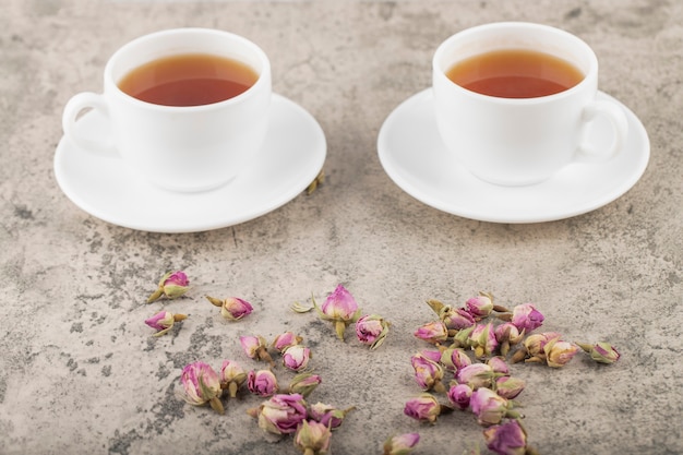 Tassen schwarzer heißer Tee mit getrockneten Rosen auf Steinoberfläche.