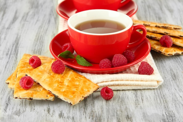 Tassen Tee mit Keksen und Himbeeren auf dem Tisch in der Nähe