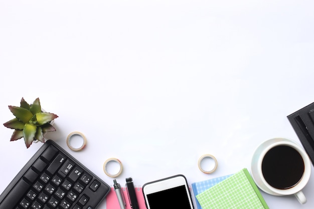 Tastatur, Smartphone, Notizbuch, Schalenkaffee, Stift und Versorgungsmaterialien setzen auf einen weißen Schreibtisch.
