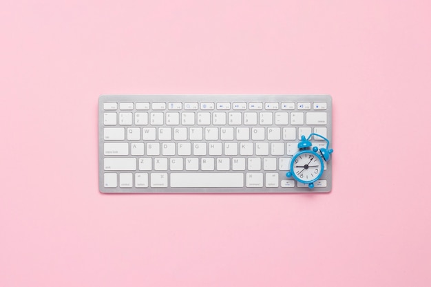 Tastatur und Wecker auf einem rosa Hintergrund. Flache Lage, Draufsicht.