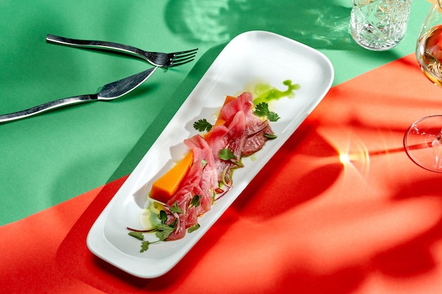 Tataki de atún con cebolla y calabaza en un plato blanco con fondos brillantes. Cocina japonesa. Enfoque selectivo, sombras duras