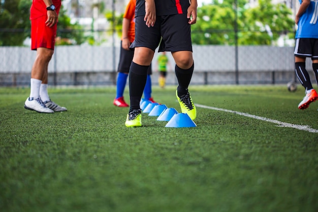 Táticas de bola de futebol no campo de grama com cone de barreira para treinar a habilidade de salto de crianças na academia de futebol