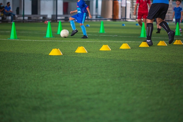 Foto táticas de bola de futebol no campo de grama com cone para treinamento em segundo plano. treinamento de crianças na academia de futebol