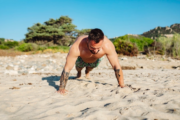 Tattoo-Mann macht Liegestütze am Strand