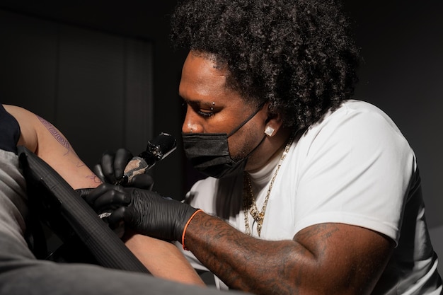 Tatuador afroamericano profesional hace un tatuaje en el brazo del cliente