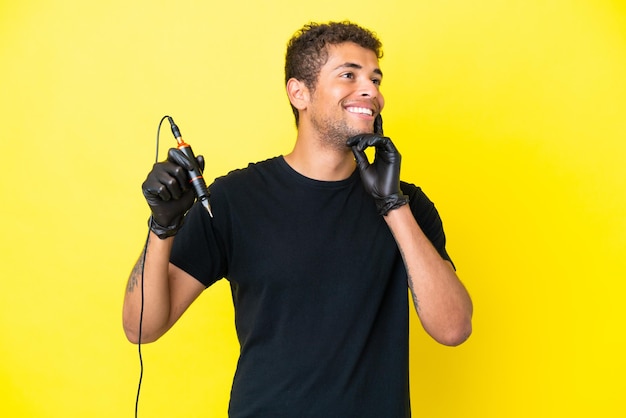 Tatuador brasileiro isolado em fundo amarelo pensando em uma ideia enquanto olha para cima