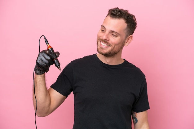 Tatuador brasileiro isolado no fundo rosa olhando para o lado e sorrindo