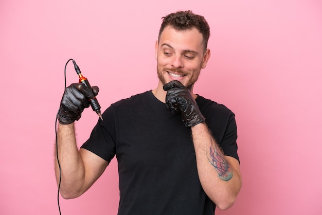 Tatuador brasileiro isolado no fundo rosa olhando para o lado e sorrindo