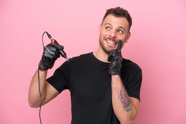 Tatuador brasileño aislado de fondo rosa pensando en una idea mientras mira hacia arriba