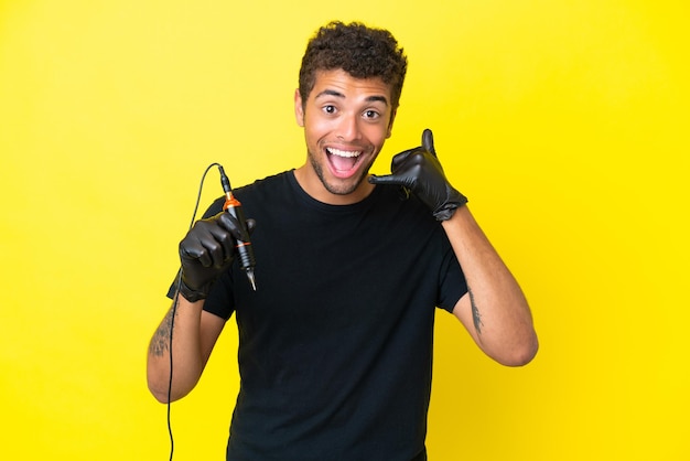 Tatuador brasileño hombre aislado sobre fondo amarillo haciendo gesto de teléfono Llámame de nuevo firmar