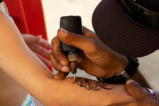 Tatuador haciendo tatuaje de henna en el brazo de una niña