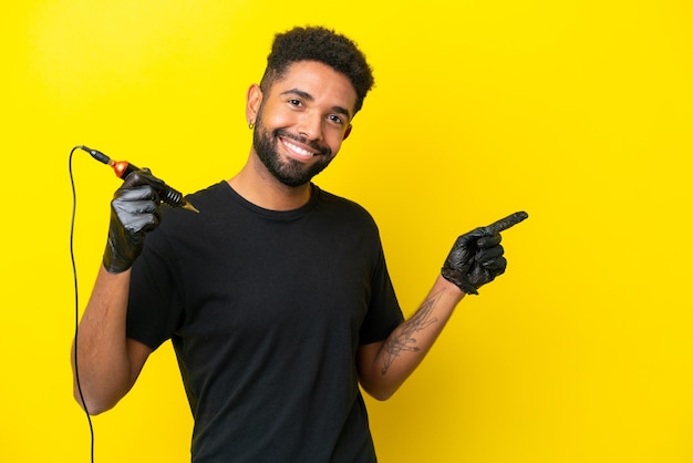 Tatuador hombre hombre brasileño aislado sobre fondo amarillo apuntando con el dedo al lado