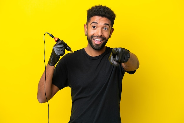 Tatuador homem brasileiro isolado em fundo amarelo surpreso e apontando para a frente