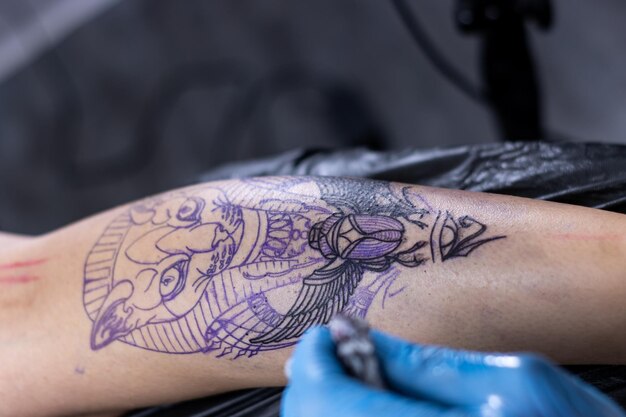 Tatuador irreconhecível com tatuagem desenhando uma máquina no corpo de uma cliente irreconhecível no salão