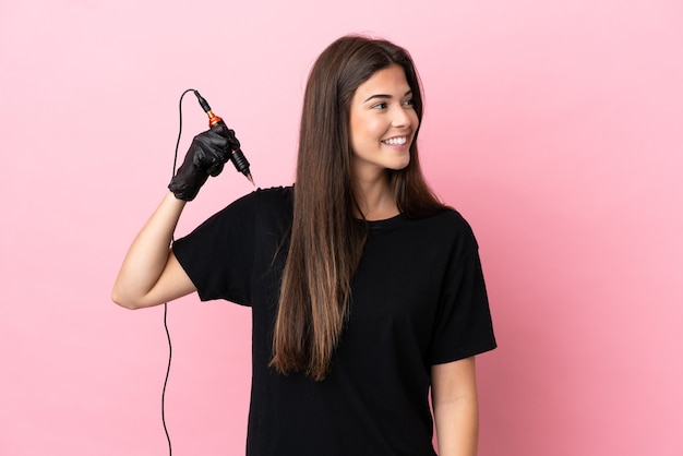 Tatuador mujer aislada sobre fondo rosa mirando hacia el lado y sonriendo