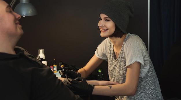 Tatuador de mujer alegre haciendo tatuaje con máquina de tatuaje en el brazo masculino. Profesión femenina inusual, espacio de copia