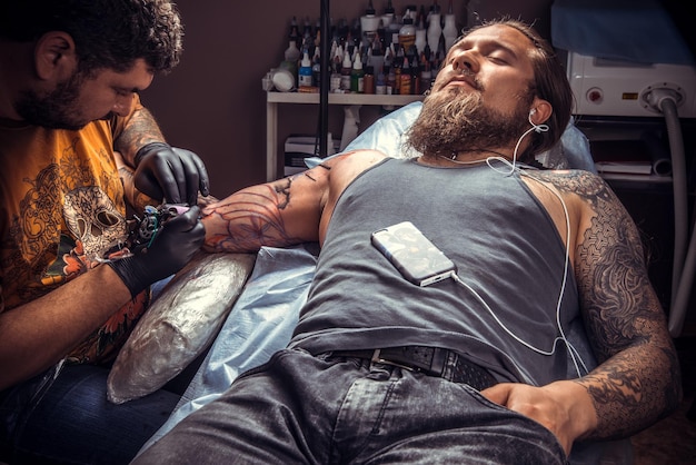 Tatuador no trabalho no estúdio de tatuagem./Homem usando luvas faz tatuagem legal no estúdio de tatuagem.