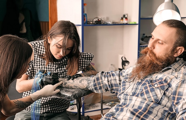 Tatuador profesional enseñando aprendiz en salón Concepto de aprendizaje