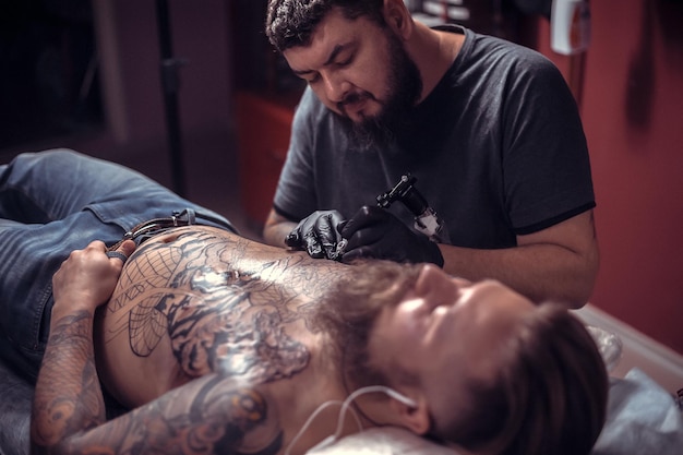 Tatuador profesional hace un tatuaje en la piel en el estudio de tatuajes./Tatuador haciendo tatuajes en el salón.