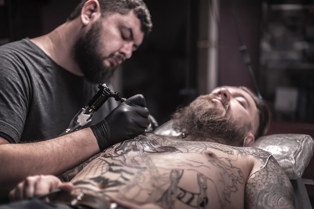 Tatuador profesional que trabaja en una ametralladora de tatuaje profesional en un estudio de tatuajes