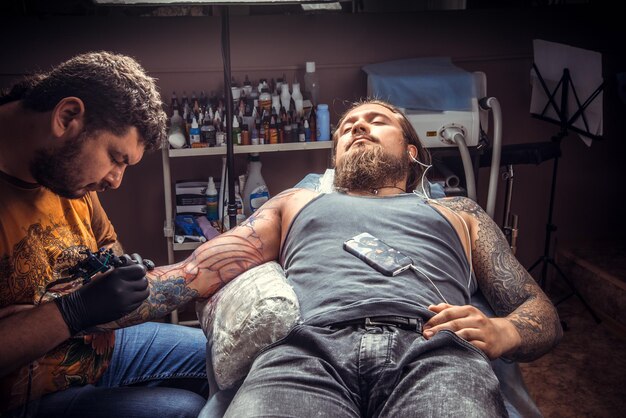 Tatuador profissional faz tatuagem no estúdio de tatuagem/homem usando luvas trabalha no salão.