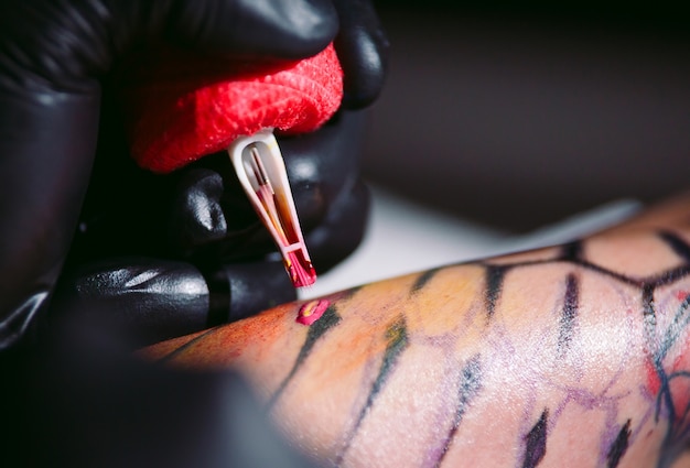 Tatuador profissional faz uma tatuagem na mão de uma jovem garota.