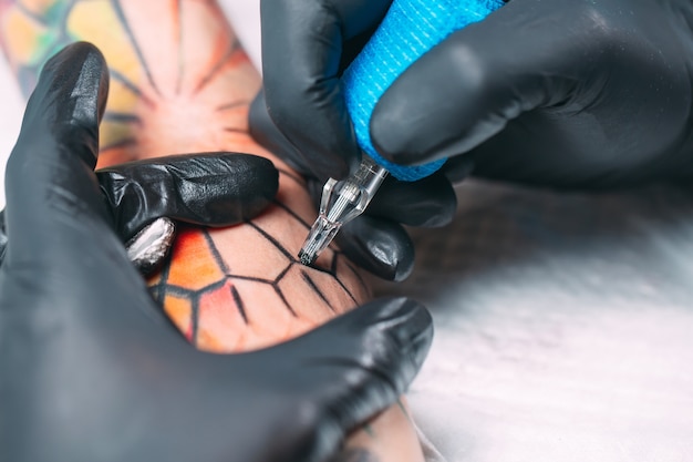 Tatuador profissional faz uma tatuagem na mão de uma jovem garota.