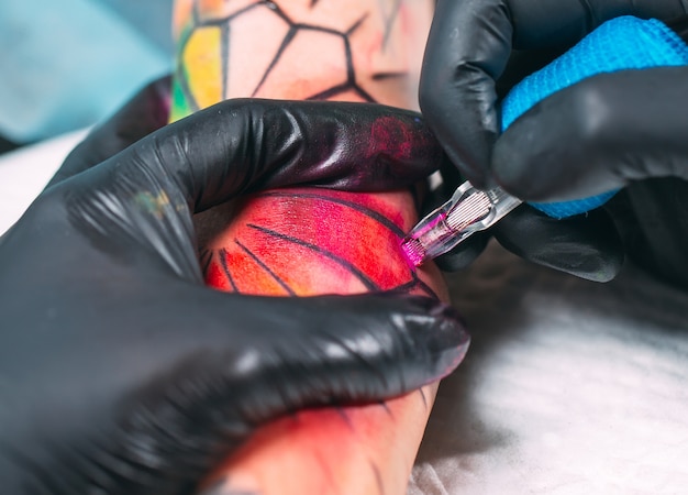 Tatuador profissional faz uma tatuagem na mão de uma jovem garota.