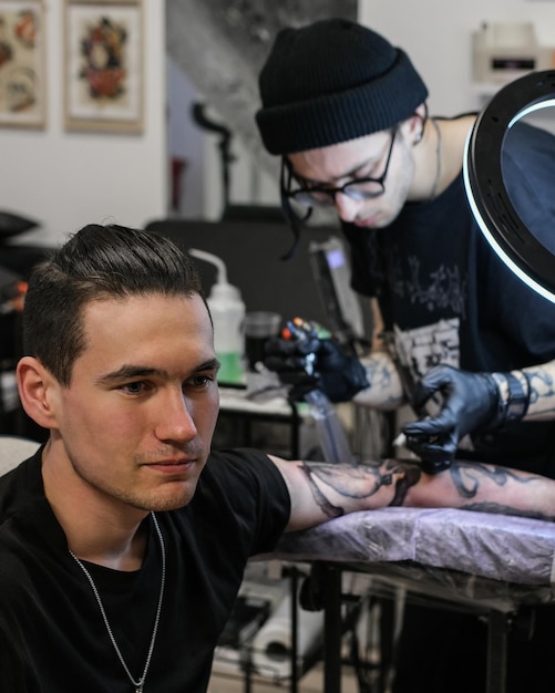 Tatuador profissional faz uma tatuagem na mão do homem tatuador no trabalho