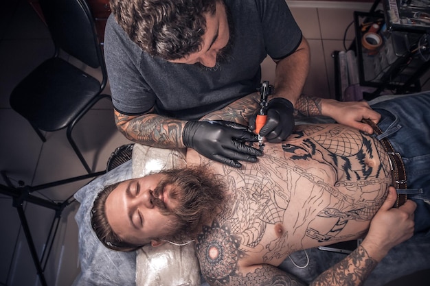 Tatuador profissional trabalhando em dispositivo de máquina de tatuagem profissional em estúdio de tatuagem Mestre de tatuagem trabalhando em metralhadora de tatuagem profissional em estúdio de tatuagem