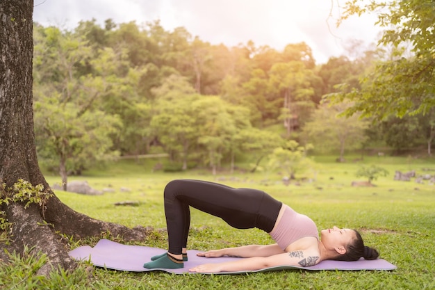 Tatuaje asiático joven haciendo yoga en el parque