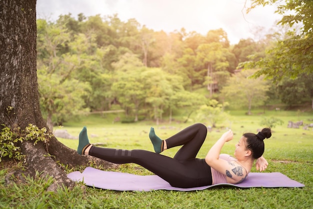 Tatuaje asiático joven haciendo yoga en el parque